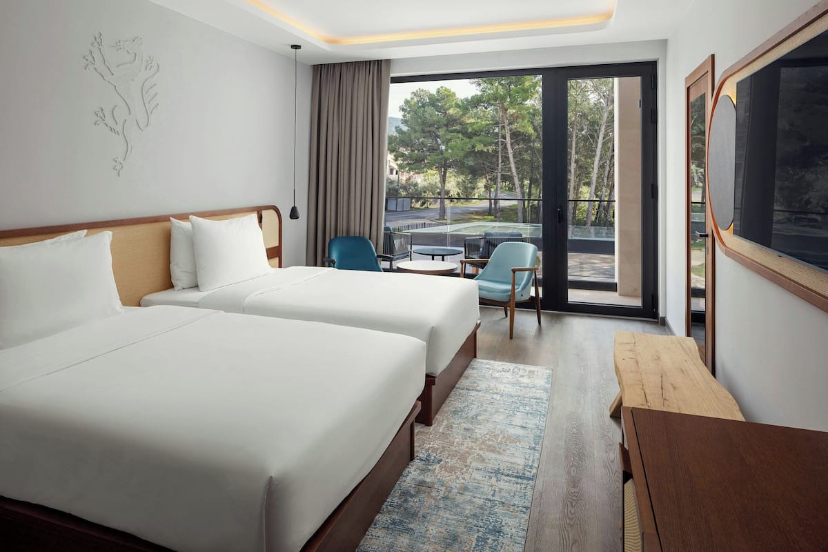 Une chambre d’hôtel avec deux lits, une table en bois, une chaise et une vue sur l’extérieur.