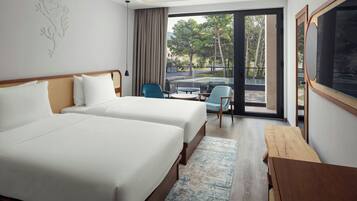 A hotel room with two beds, a wooden table, a chair, and a view of the outdoors.