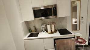 Pieni, käytännöllinen keittiö, jossa on valkoiset kaapit, mikroaaltouuni, kahvinkeitin ja pieni pesuallas.
