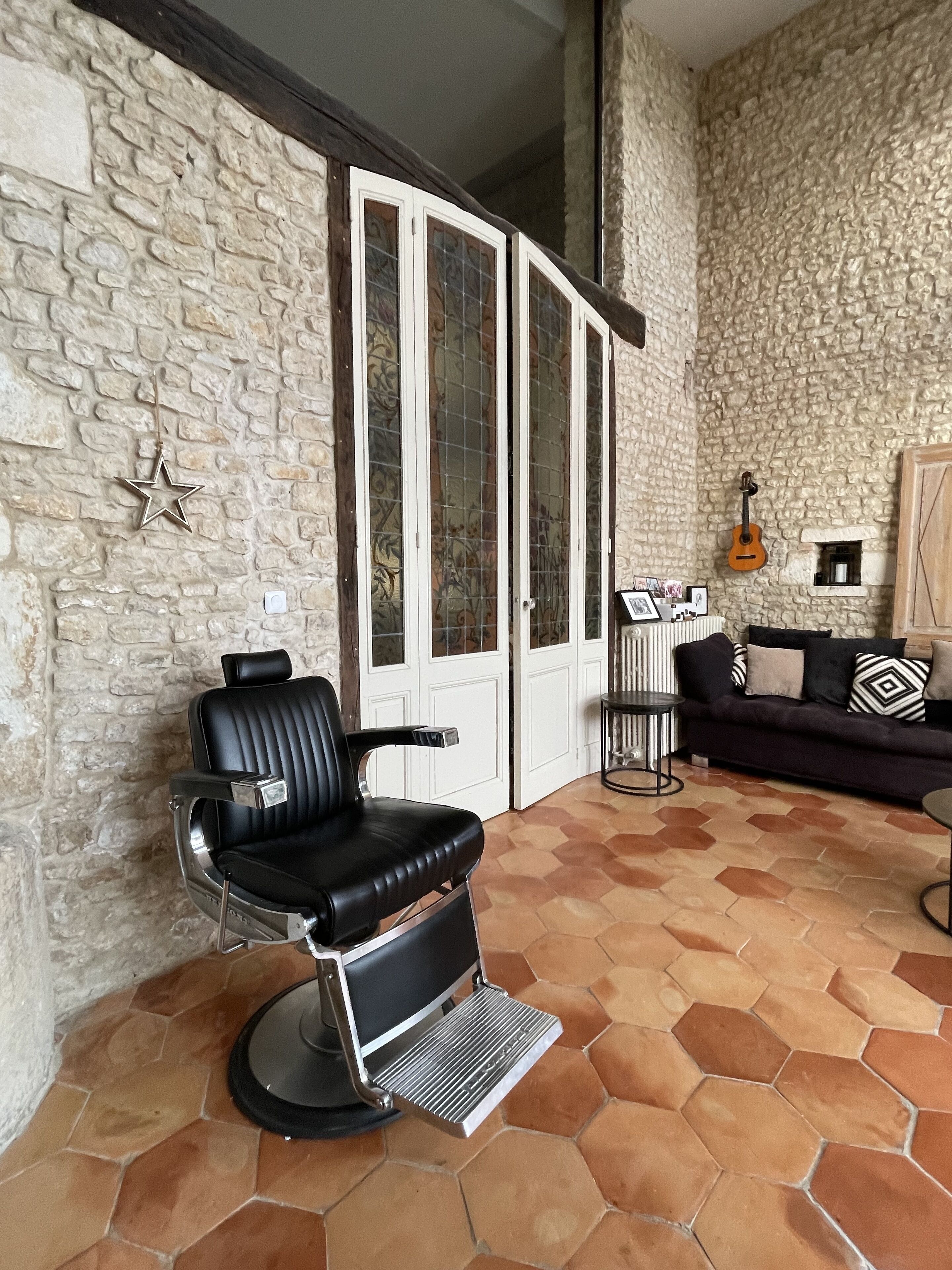 A living room with a stone wall, a black leather chair, a black sofa, and a tiled floor.