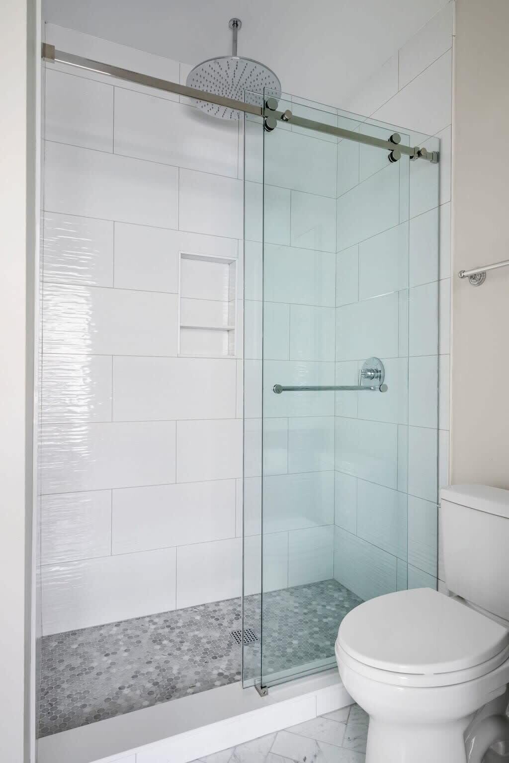 A modern bathroom with a glass shower enclosure, a toilet, and a tiled floor.