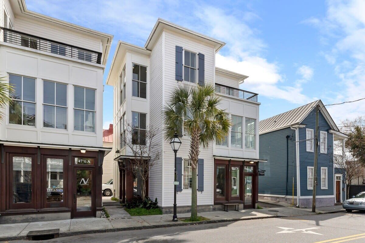 Una hilera de casas urbanas modernas con grandes ventanales, una palmera pequeña y vista a la calle.