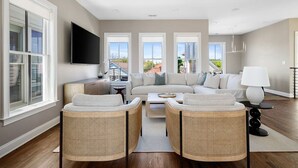 A spacious living room with a large sofa, two wicker chairs, a coffee table, and a flat-screen TV mounted on the wall. - 3 Luxury Houses w/ Patios | 1 Block from King St (Charleston)