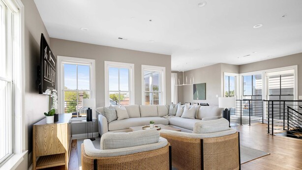 A spacious living area with a large sectional sofa, wicker chairs, and a flat-screen TV mounted on the wall. - 3 Luxury Houses w/ Patios | 1 Block from King St (Charleston)