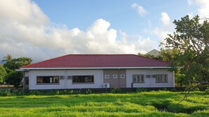 A single-story house with a red-tiled roof and a flat facade, surrounded by a well-maintained grassy field. - Mayon View Garden Apartelle Sa Bukid (Legazpi)