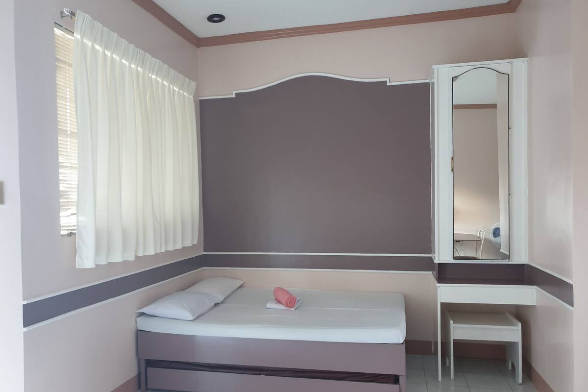 Een slaapkamer met een bed, nachtkastje, spiegel en een raam met gordijnen.