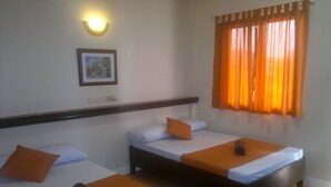 A hotel room with two single beds, each with an orange blanket and pillow. There is a framed picture on the wall above the beds, and a window with orange curtains. - Mayon View Garden Apartelle Sa Bukid (Legazpi)