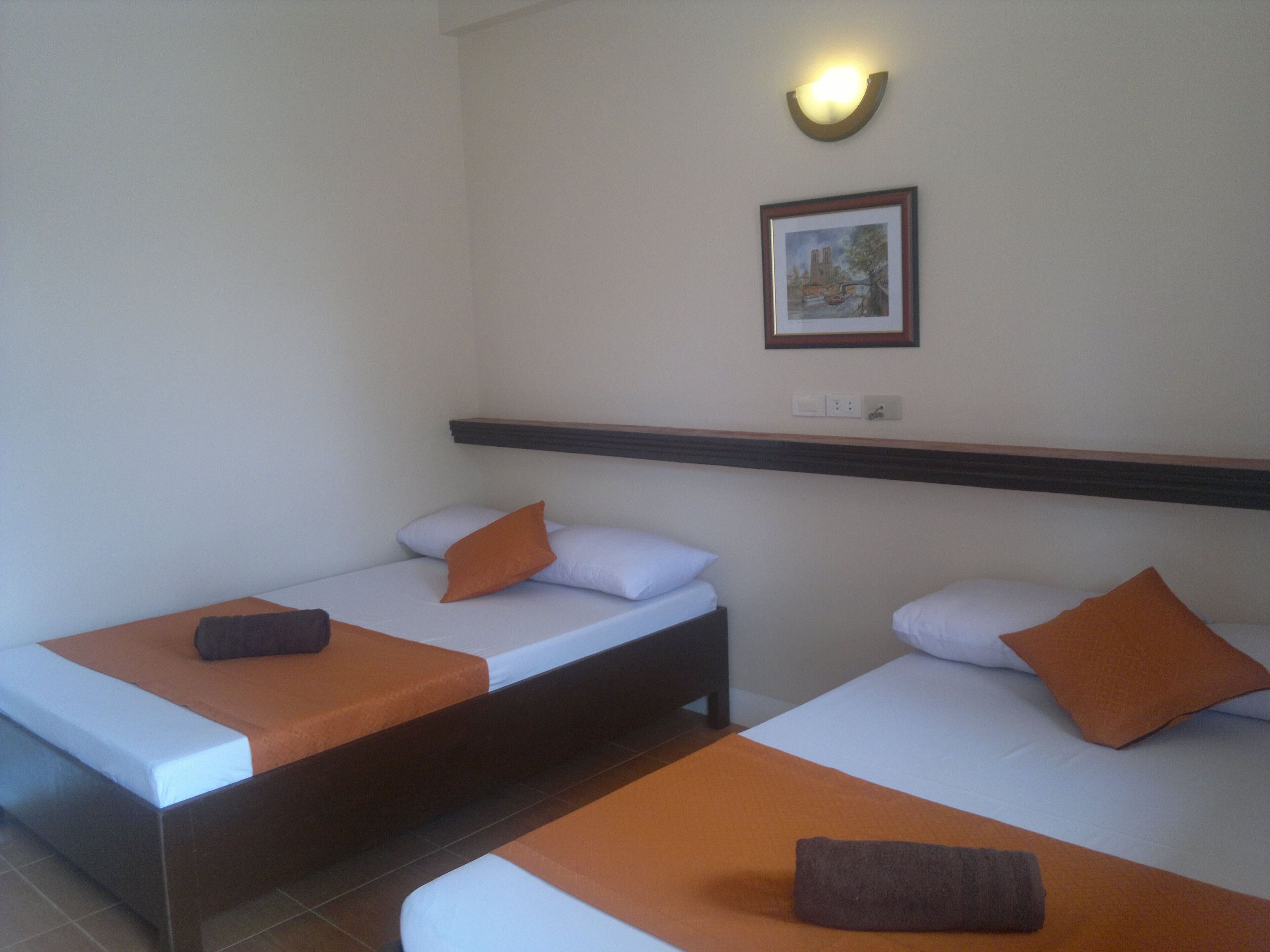 Habitación de hotel con dos camas individuales, cada una con una almohada y una toalla doblada.