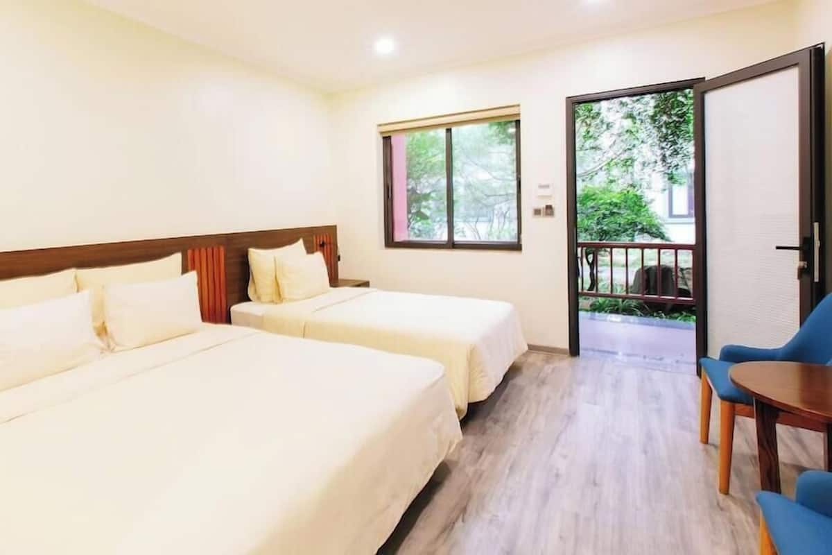 Une chambre d’hôtel avec deux lits, une petite table et un balcon donnant sur un espace verdoyant.