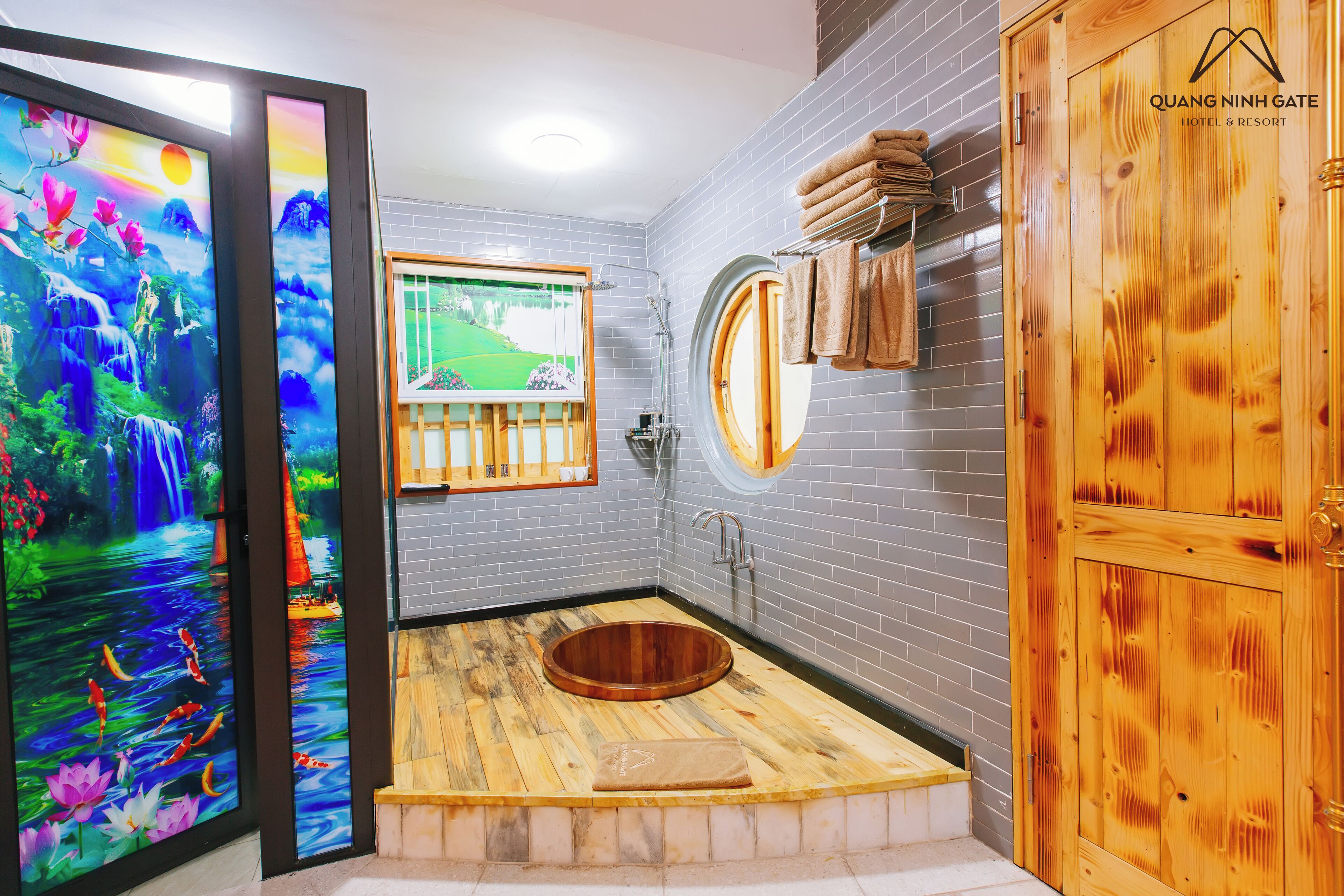 A modern bathroom with a wooden bathtub, a large mirror, and a view of a garden through a window.