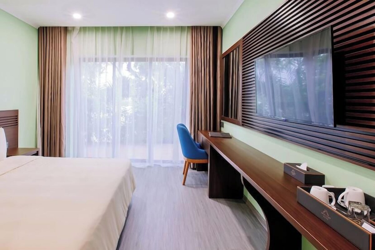 Een hotelkamer met een bed, bureau, stoel en een groot raam met gordijnen.