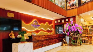 Zona de recepción de un hotel con un mostrador de madera, un televisor y un arreglo floral.