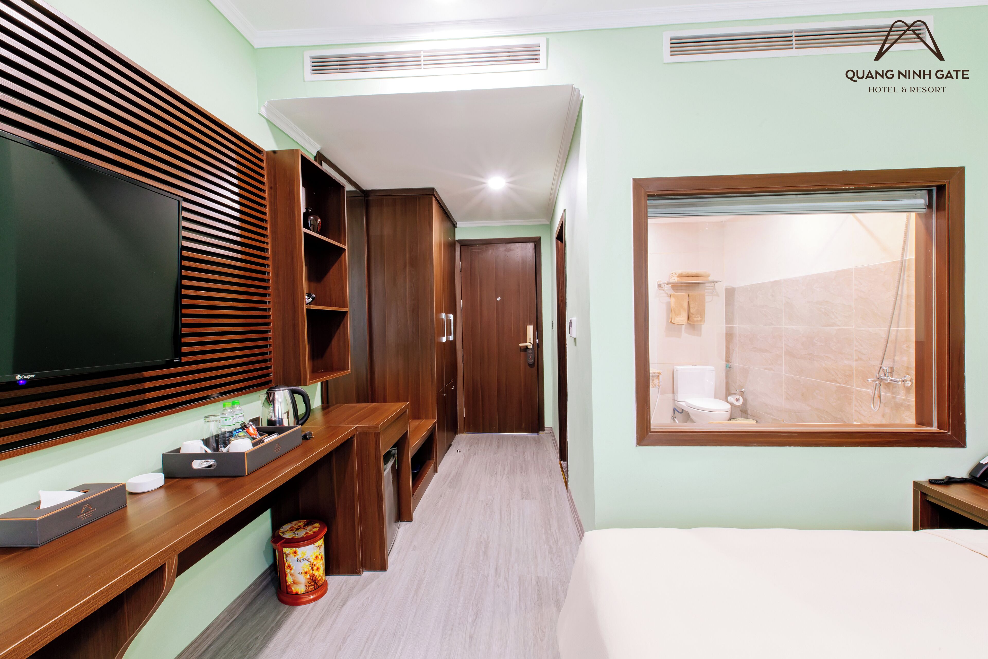Habitación de hotel con televisor, muebles de madera, baño con ducha y ventana.