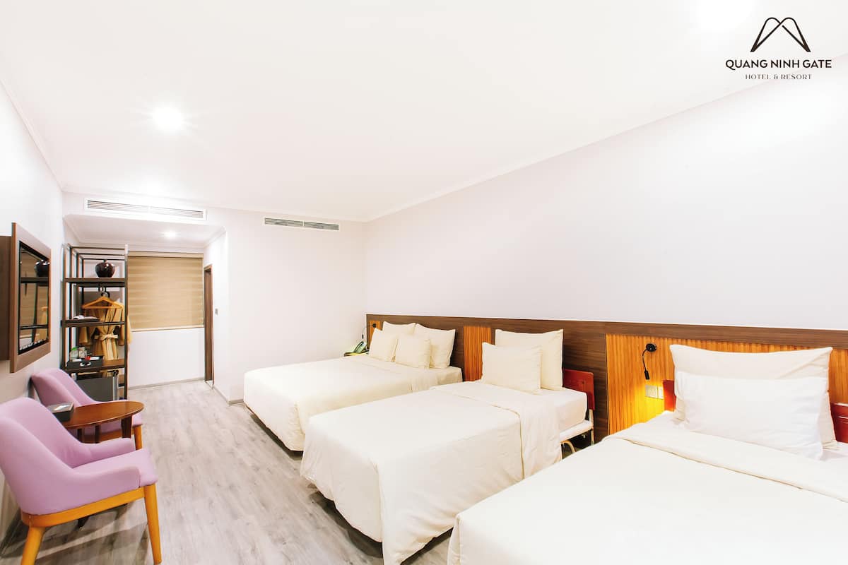 Une chambre d’hôtel avec trois lits, un bureau, une chaise et une armoire.