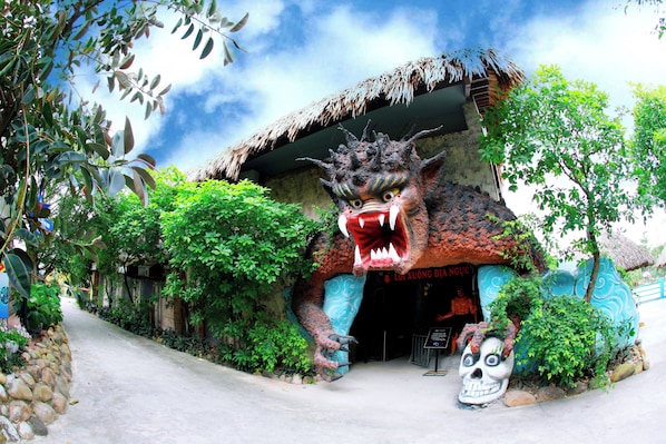 A building with a thatched roof entrance, surrounded by lush greenery. - Quang Ninh Gate Hotel & Resort (An Sinh)