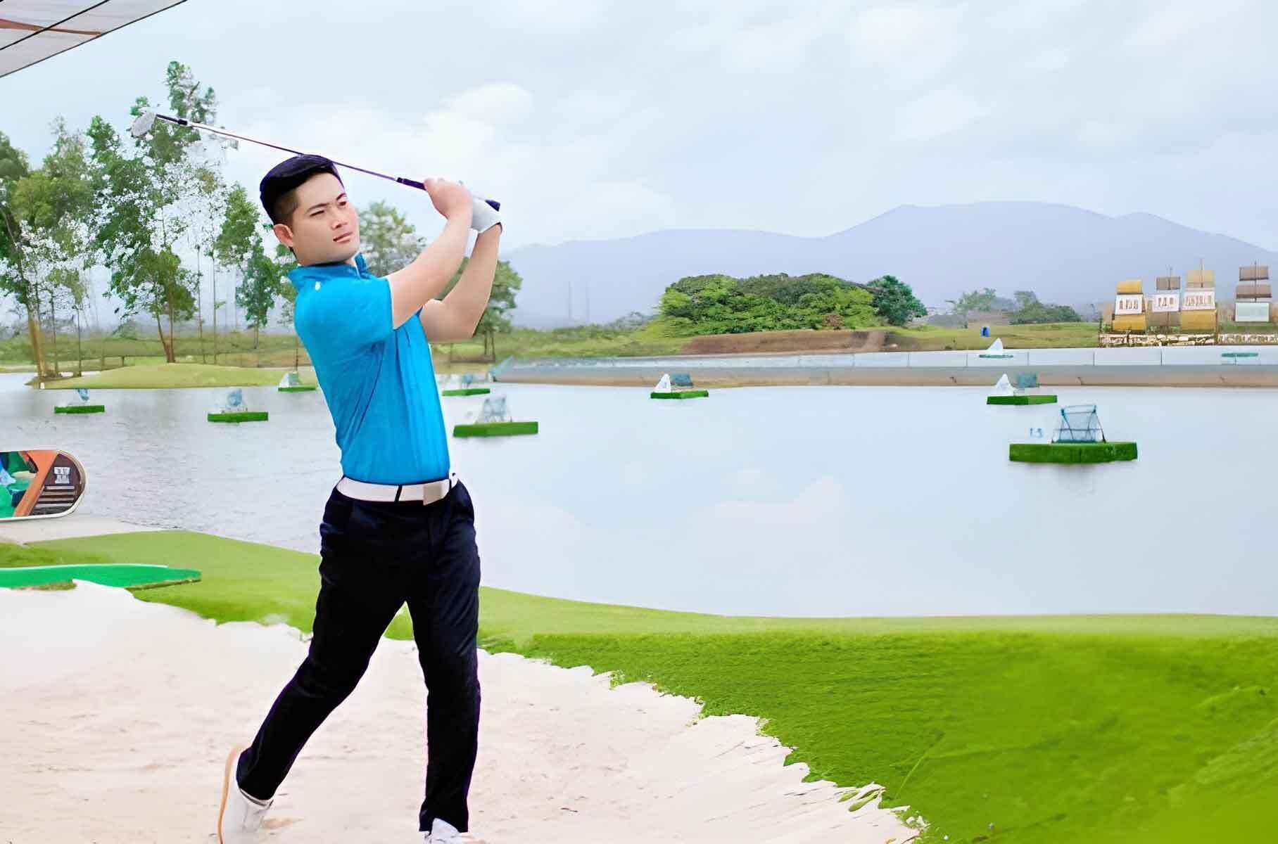 A person playing golf on a course with water hazards and distant mountains.