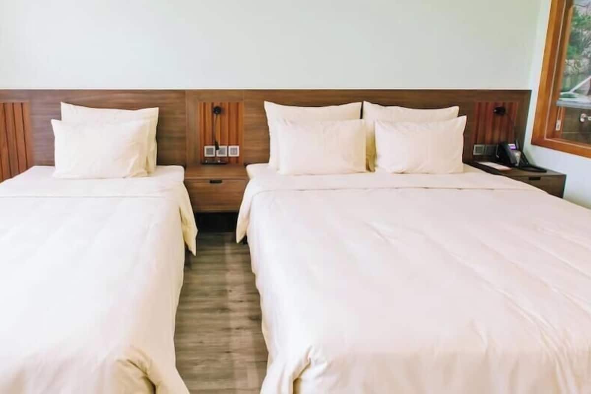 Une chambre d’hôtel avec deux lits, des têtes de lit en bois et une table de chevet avec une lampe.