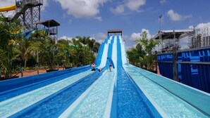 Een waterpark met meerdere glijbanen, palmbomen en een heldere lucht.