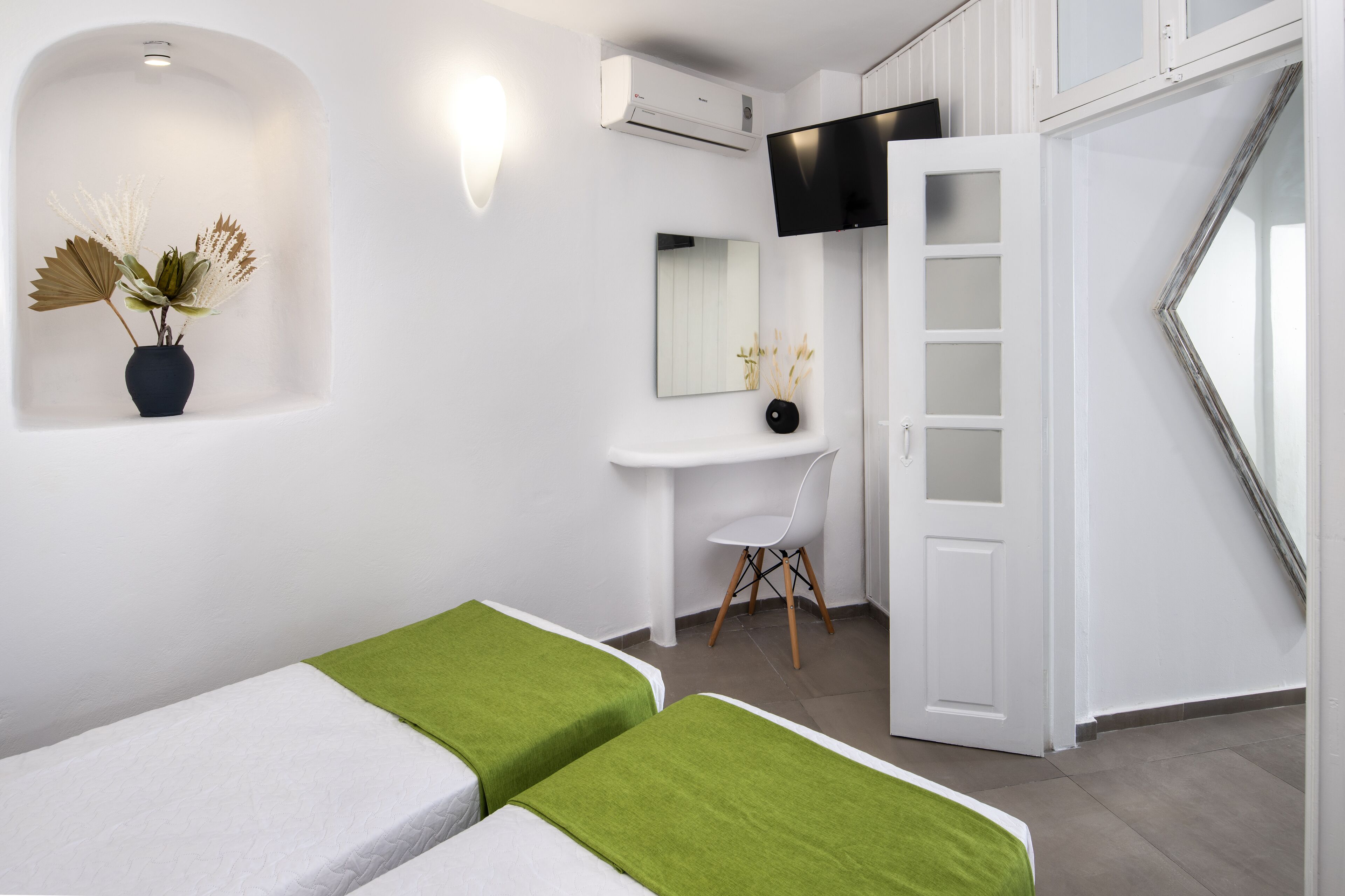 Una habitación moderna con dos camas, un escritorio, una silla, un televisor y un espejo.