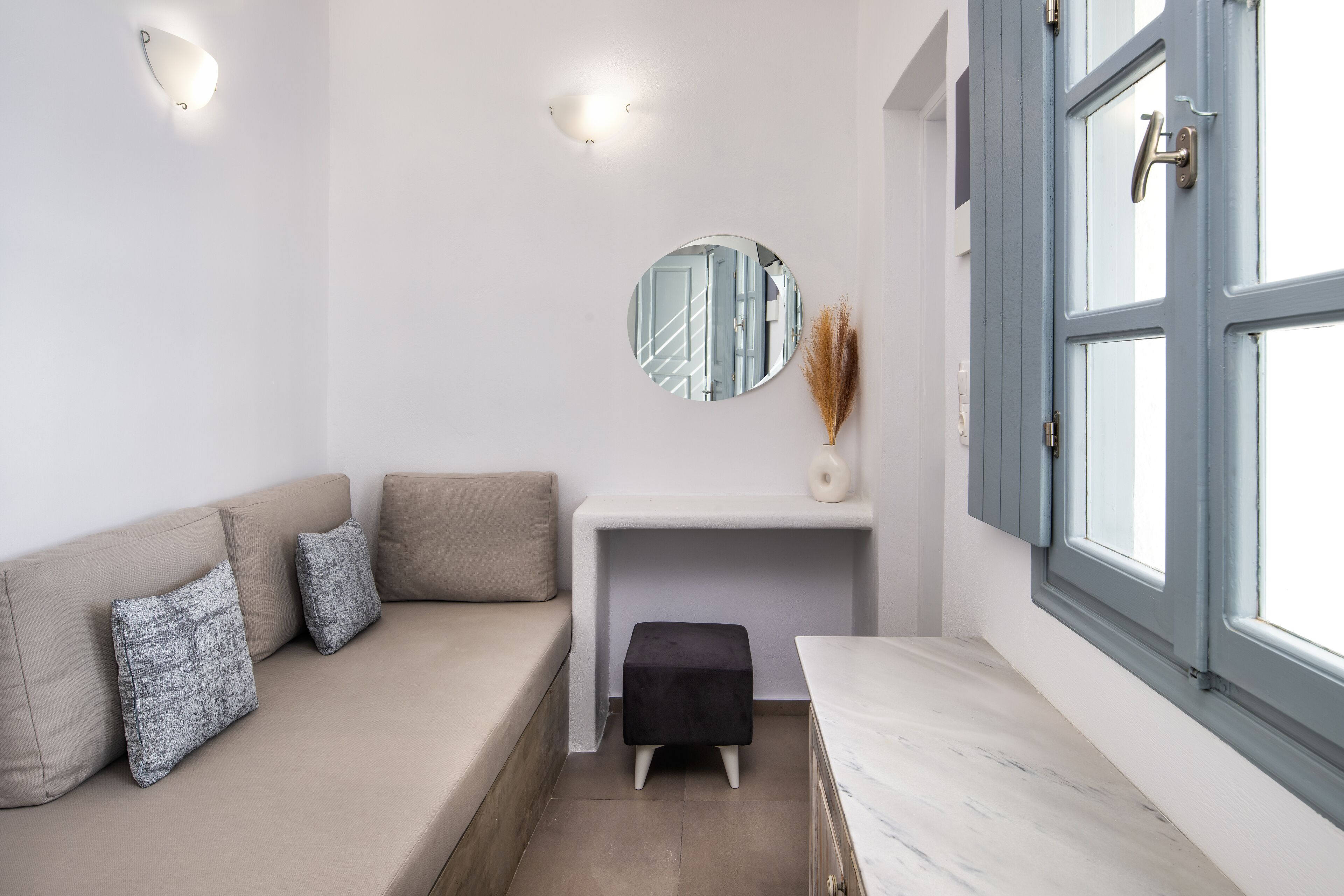Een modern interieur met een beige bank, een klein zwart voetenbankje, een ronde spiegel en een witte console tafel.