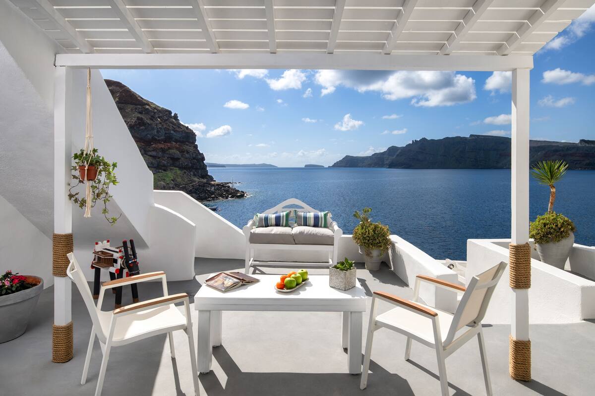 A white outdoor seating area with a table, chairs, and potted plants.