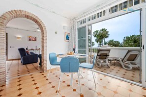 A modern living room with a dining area, featuring a brick archway, a sofa, a table with chairs, and a view through large glass doors to the outside. - Rabat 6 - El Oasis de Capistrano! (Nerja)