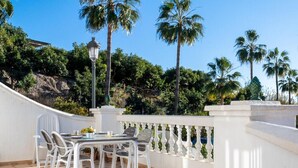 Een terras met een tafel en stoelen, omgeven door een witte balustrade en palmbomen.