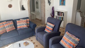 Een woonkamer met een blauwe zithoek, een rond bijzettafeltje en een boekenkast.
