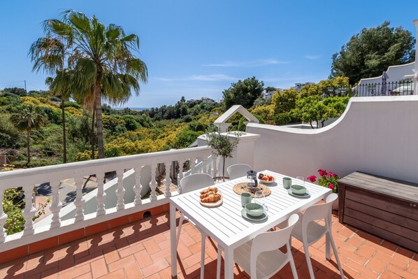 A terrace with a white table set for two, a palm tree, and a view of the landscape.