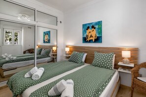 A hotel room with two beds, a large mirror, a painting, and a wicker chair.