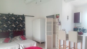 A bedroom with two beds, a red chair, a desk with a chair, and a wardrobe.