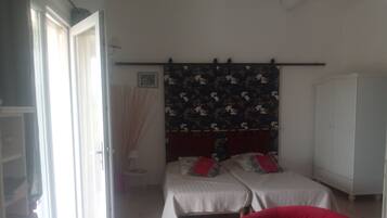 A bedroom with two beds, a wardrobe, a red chair, and a window with curtains.
