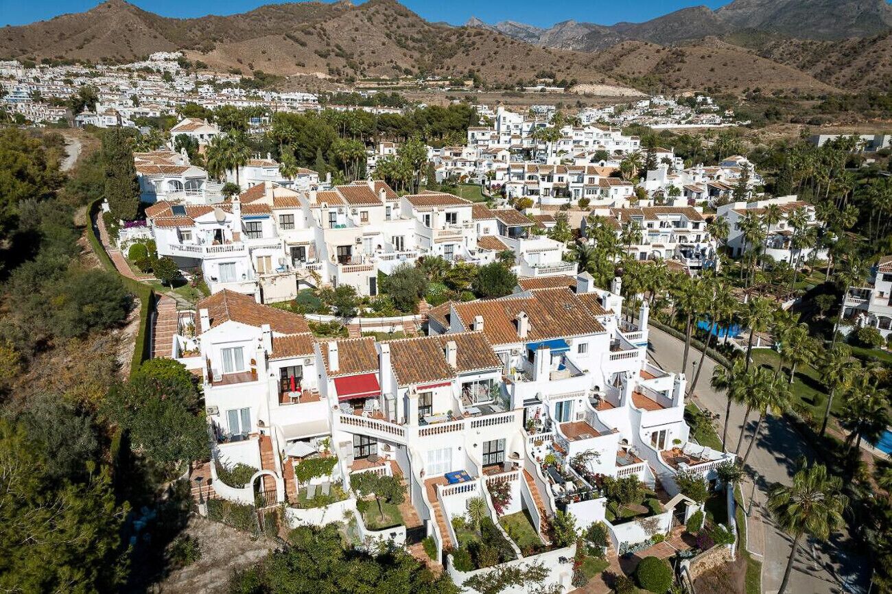 Un pueblo costero con edificios blancos, palmeras y una montaña al fondo.