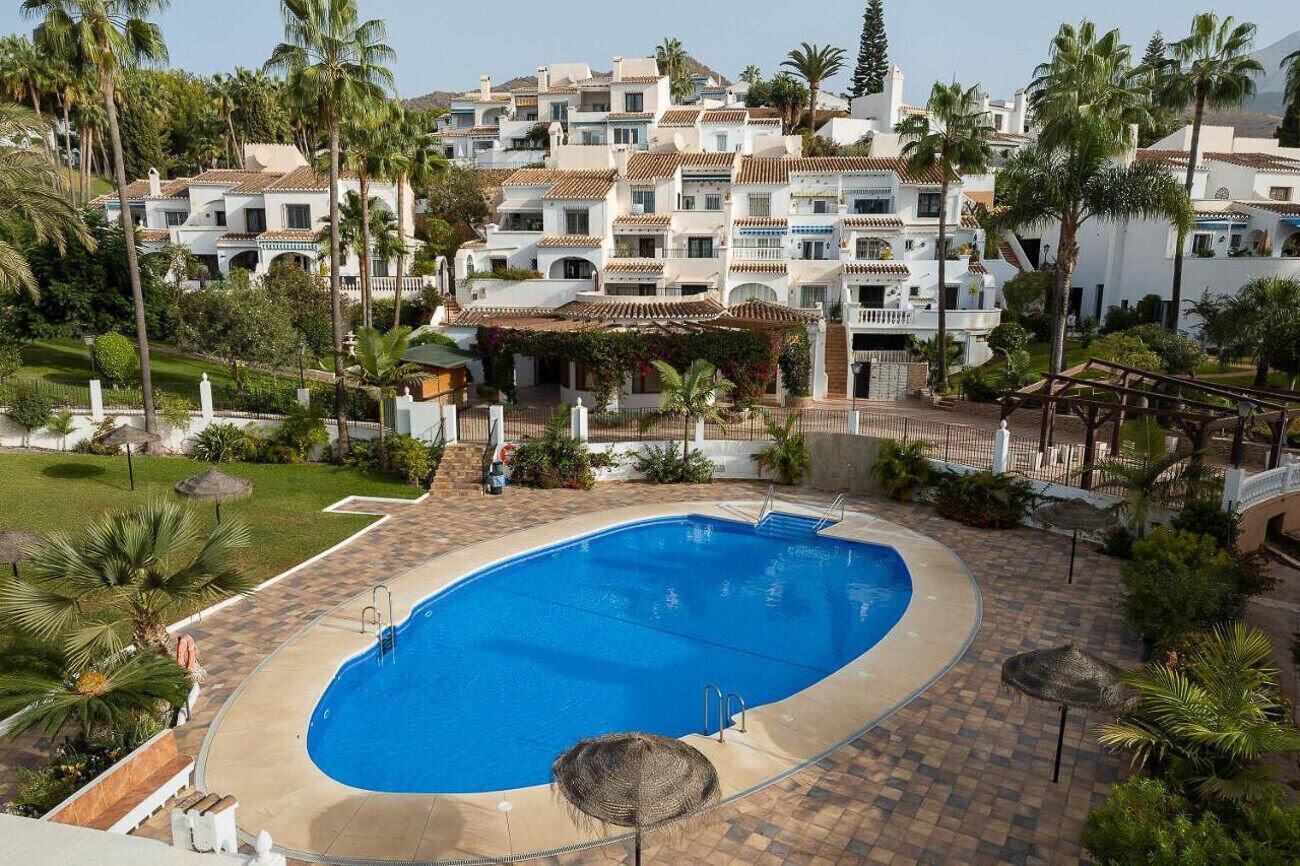 A swimming pool surrounded by palm trees and a white building with multiple balconies.
