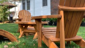 Two wooden Adirondack chairs and a small table set on a grassy lawn.