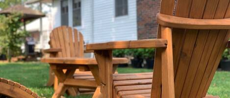Zwei hölzerne Adirondack-Stühle und ein kleiner Tisch stehen auf einer grünen Rasenfläche.