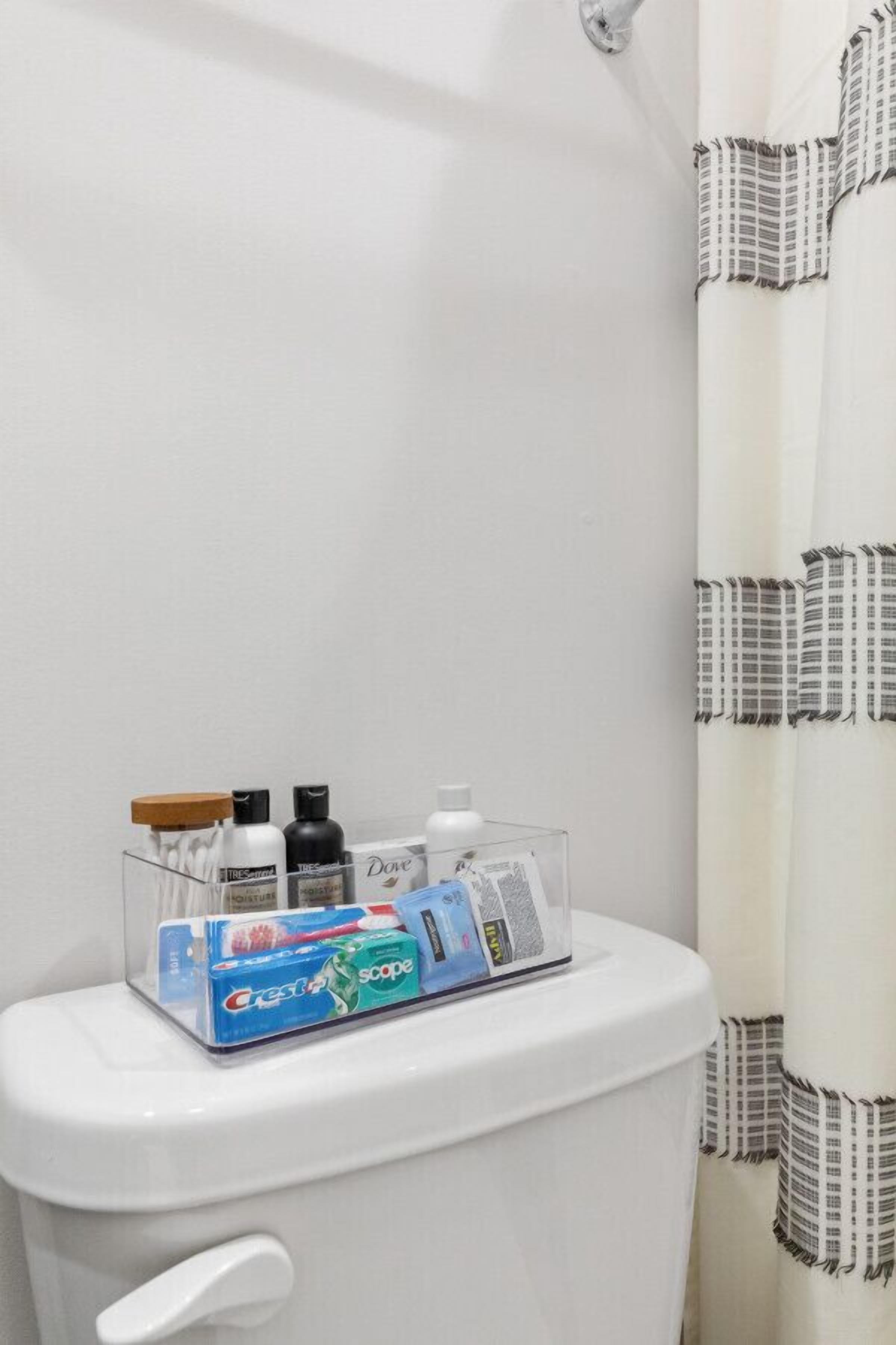 Une salle de bain équipée de toilettes, d’un rideau de douche et d’une boîte de rangement contenant des articles de toilette.