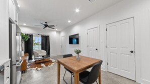 A modern kitchen with white cabinets, a refrigerator, and a dining area with a wooden table and chairs. - Creole House*KING bed*Relax in Cajun Comfort! (Lafayette)
