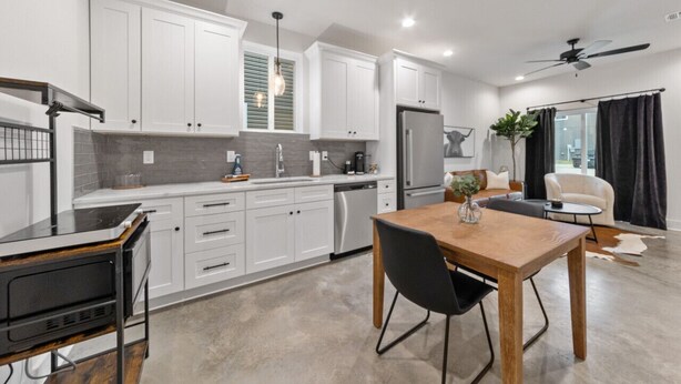A modern kitchen with white cabinets, a built-in oven, and a dining area with a wooden table and black chairs. - Creole House*KING bed*Relax in Cajun Comfort! (Lafayette)