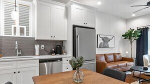 A modern kitchen with white cabinets, a stainless steel refrigerator, and a dining area with a wooden table and black chairs. - Creole House*KING bed*Relax in Cajun Comfort! (Lafayette)