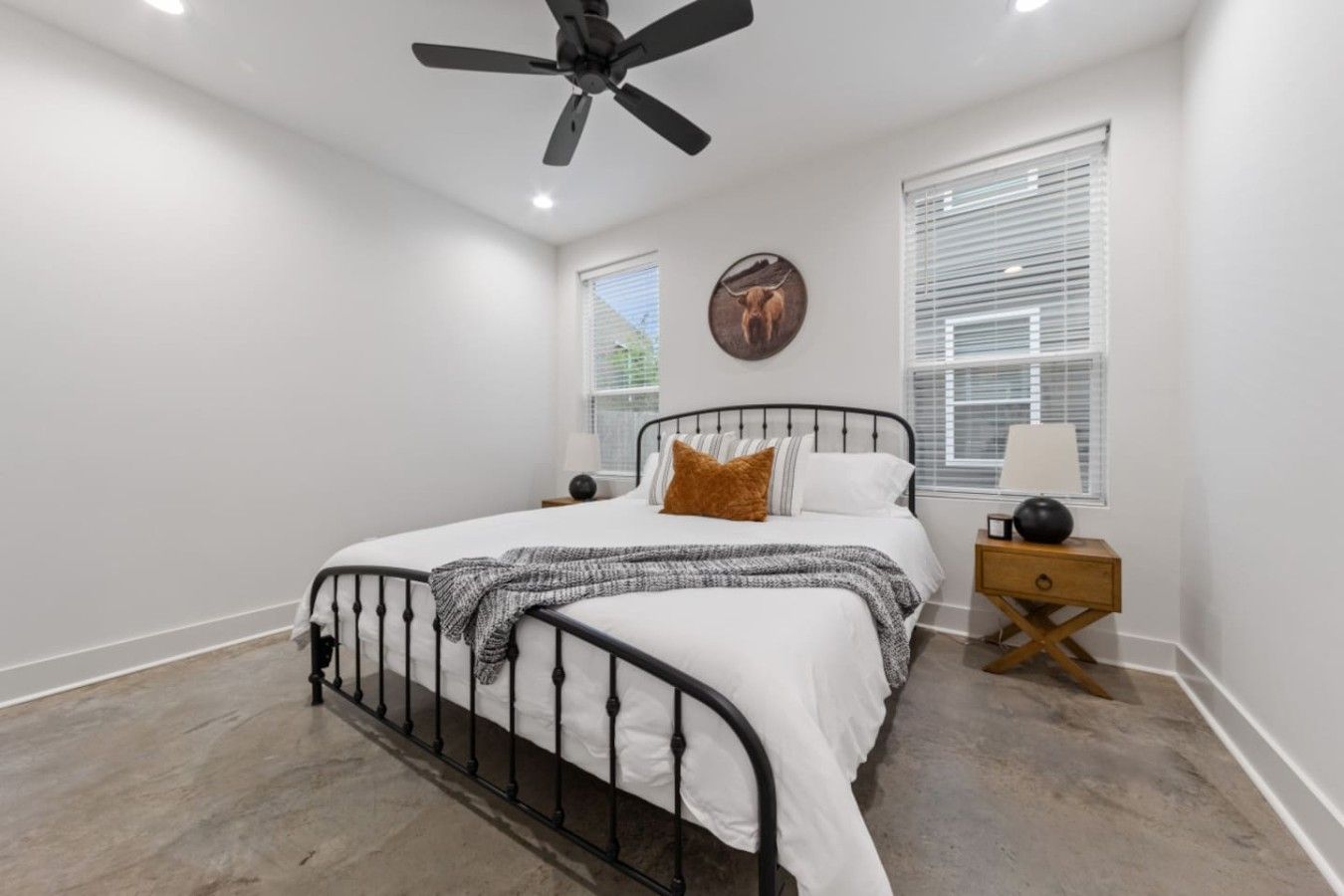 Une chambre à coucher avec un lit, un ventilateur de plafond, une table de chevet et une fenêtre avec des stores.