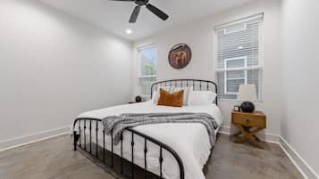 Une chambre à coucher avec un lit, un ventilateur de plafond, une table de chevet et une fenêtre avec des stores.