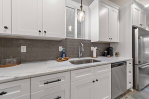 A kitchen with white cabinets, a stainless steel refrigerator, a sink, and a hanging light fixture.