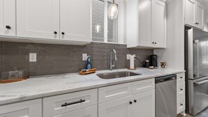 A modern kitchen with white cabinets, a stainless steel refrigerator, and a marble countertop. - Creole House*KING bed*Relax in Cajun Comfort! (Lafayette)
