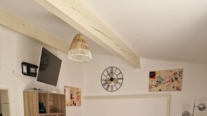 Una habitación con piso a cuadros, un sofá rojo con estampado, un mueble de madera, una mesita pequeña, un televisor montado en la pared y una lámpara de pie.