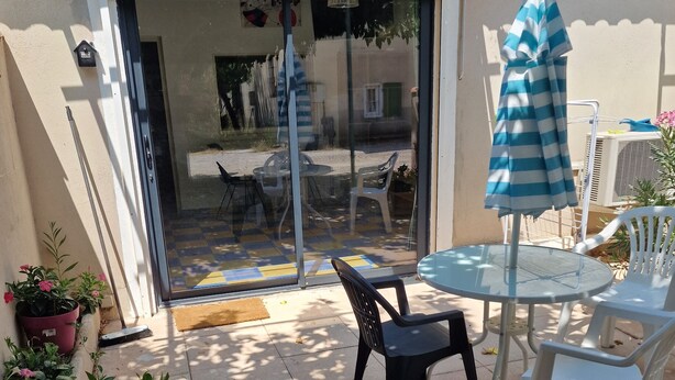 Un patio con puerta de vidrio que da a una zona de estar al aire libre, una pequeña mesa y un parasol a rayas.