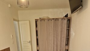 Una cama bien hecha con una toalla azul doblada, un cabecero de madera, una puerta blanca, un estante pequeño y un televisor montado en la pared.