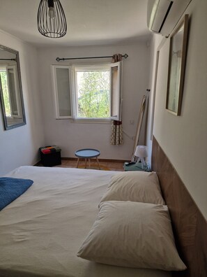 Relax in this serene space with a large bed, a window overlooking lush greenery, and a cozy reading nook.