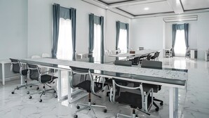 Un salón de conferencias moderno con una larga mesa, varias sillas y ventanas grandes con cortinas.