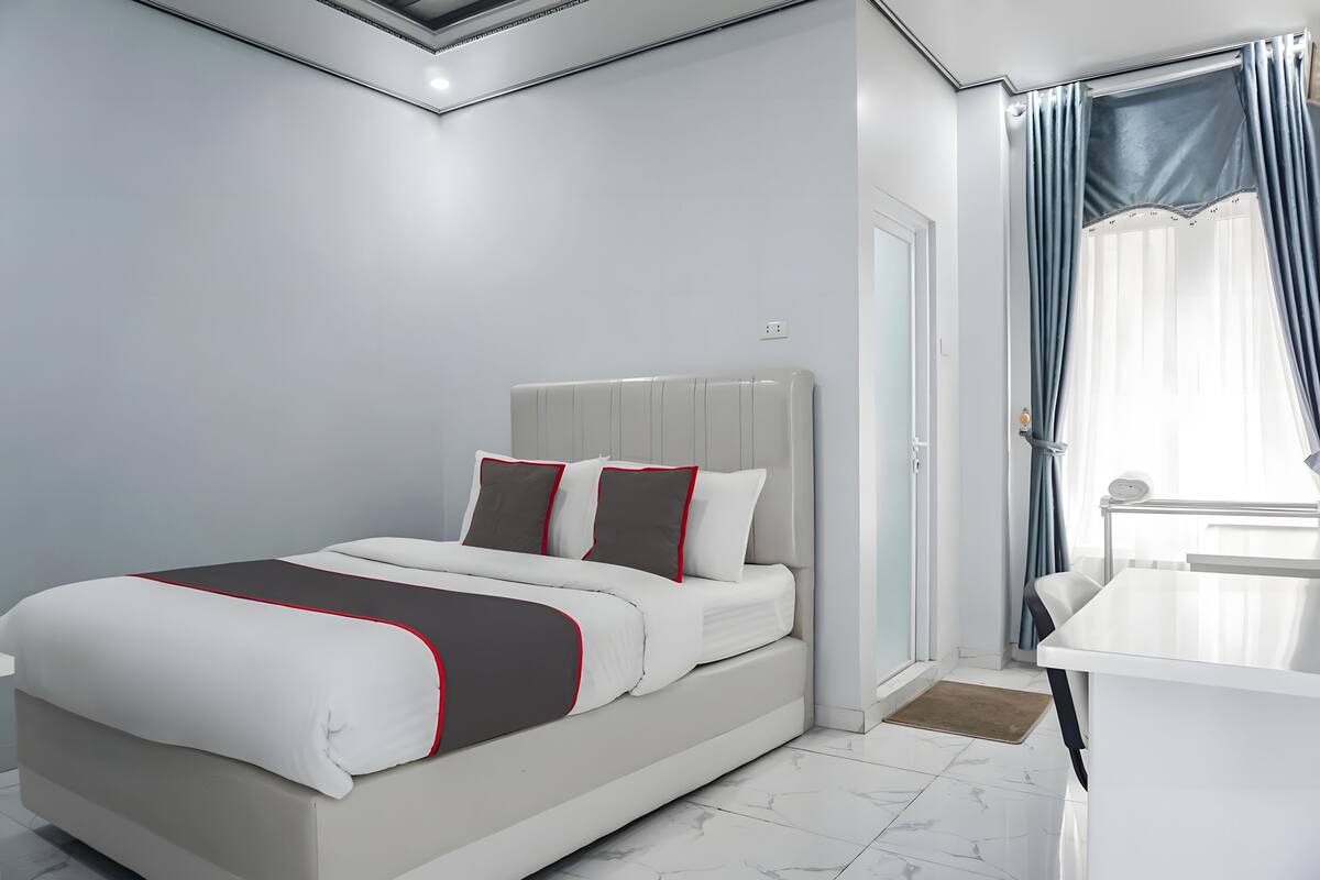 A modern bedroom with a bed, a bedside table, and a view of the outdoors through a window with curtains.